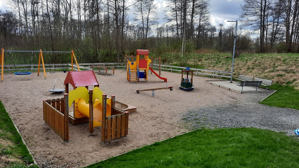 Foto över en färgglad lekplats, underlaget är av sand och runt om växer det gräs.