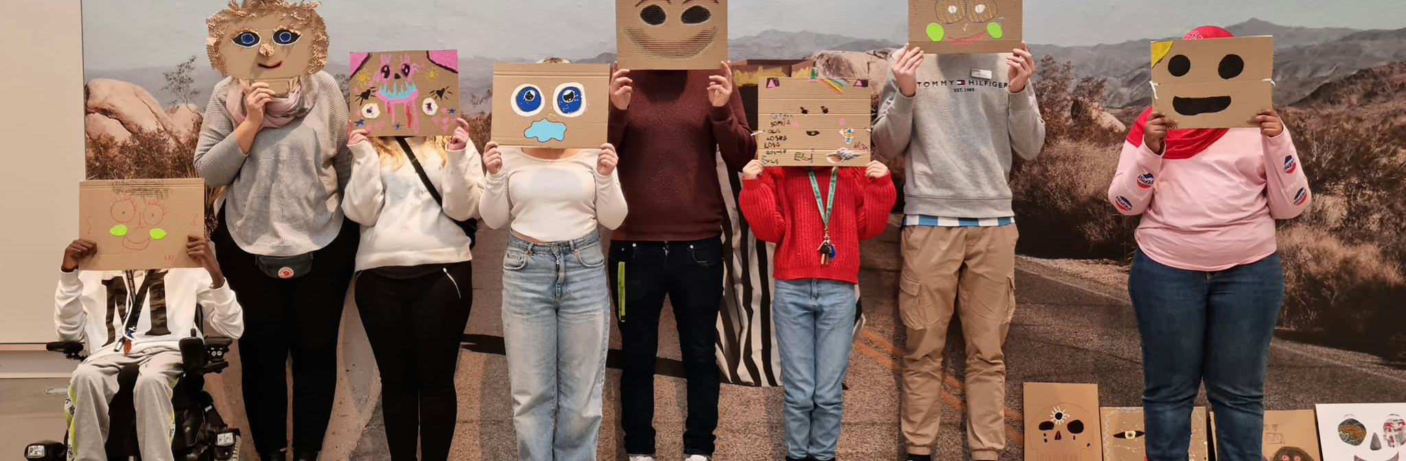 En grupp står och håller fram masker framför ansiktet som de själva skapat i ateljén