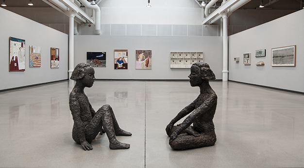 Två skulpturer, flickor, sitter vända mot varandra. 