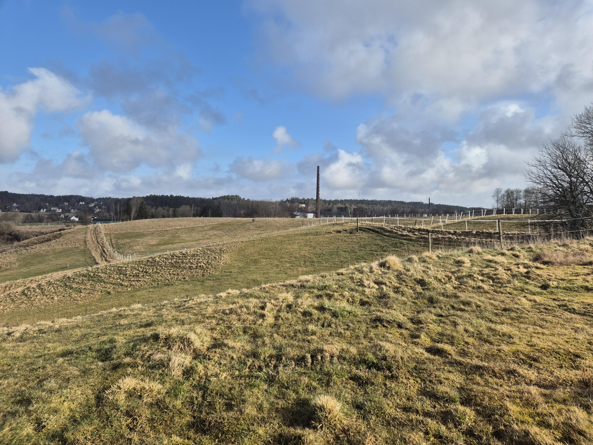 Ett backigt fält, med skorstenen från Sjuntorps fabriker i bakgrunden