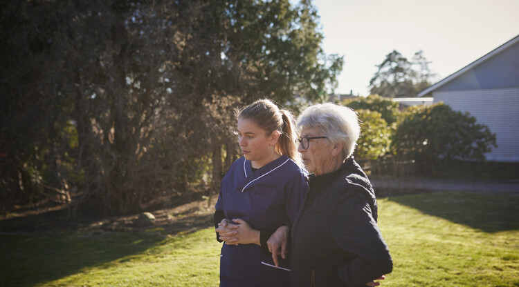 En person från hemtjänsten promenerar med en äldre utomhus