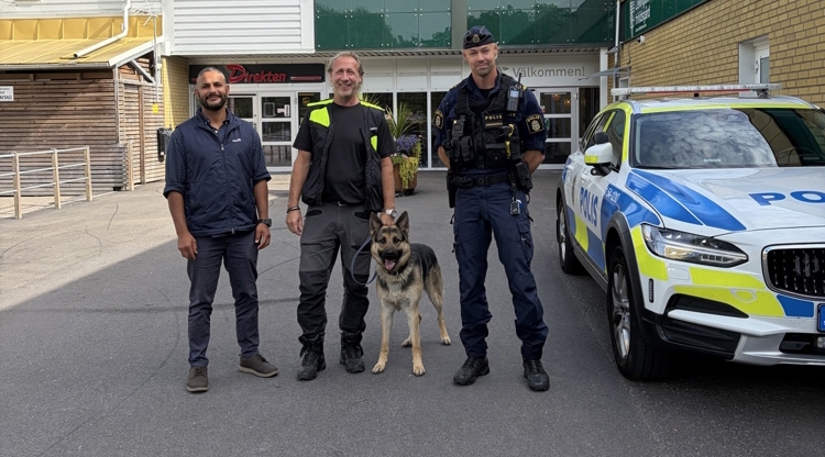 tre personer står framför en byggnad. Uniformerad polis och en polishund. 