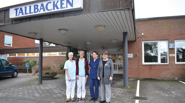 Fyra kvinnor som jobbar på Tallabackens demenscentrum står utomhus utanför entrén där det står Tallbacken.