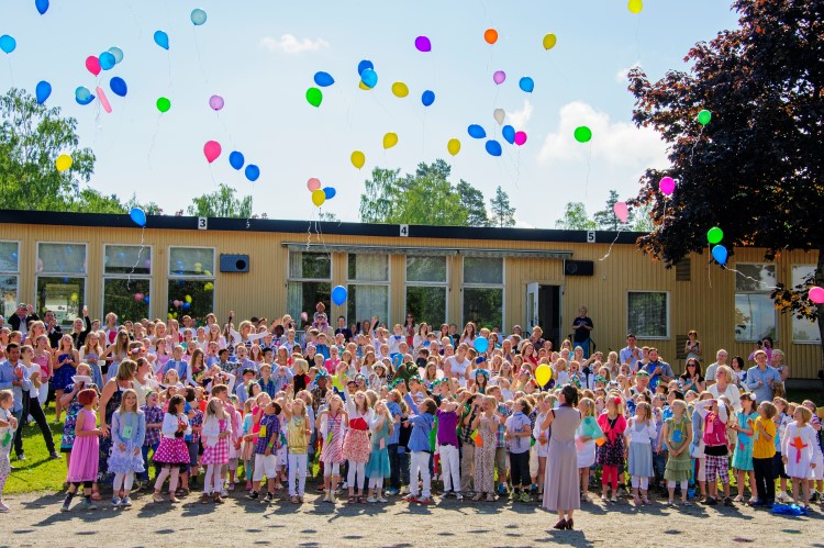 skolklass i sommarkläder släpper blå och gula ballonger framför skolan