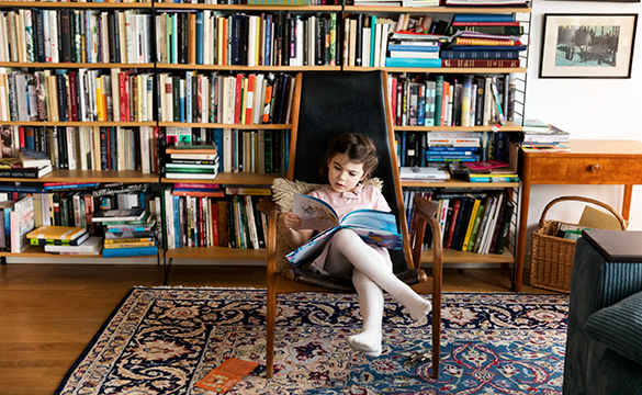 Flicka sitter i stol och läser. Foto.