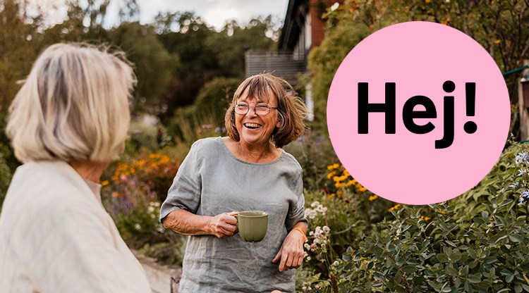 Två kvinnor i en trädgård som ler och har en kopp i handen.