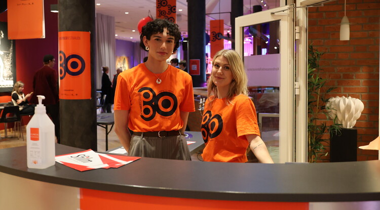 Två personer tar emot besökare under festival.