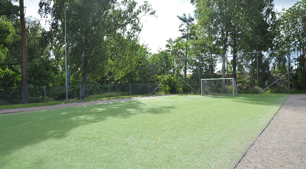 Bilden föreställer en fotbollsplan med konstgräs. På sidan av planen finns gruspartier. 