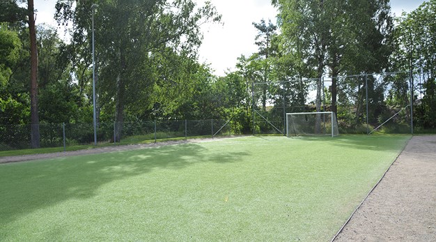 Bilden föreställer en fotbollsplan med konstgräs. På sidan av planen finns gruspartier. 