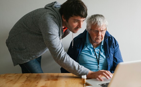 En äldre man får hjälp av en annan person med sin dator. Foto.