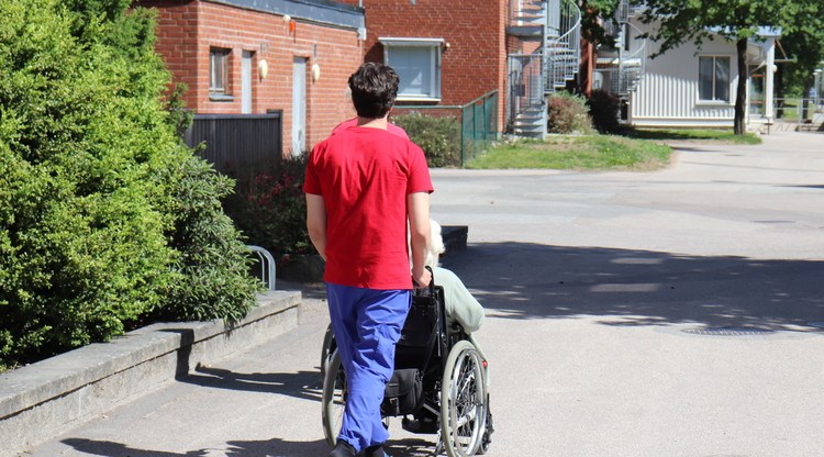 Personal ute på promenad med person i rullstol.