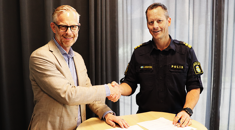två män skakar hand och ler mot kameran. En har polisuniform