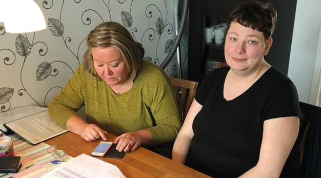 En boendestödjare visar en brukare hur telefonen kan användas som hjälpmedel.
