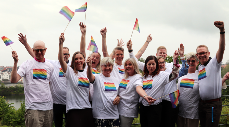 Flera glada personer i pridetröjor med prideflaggor