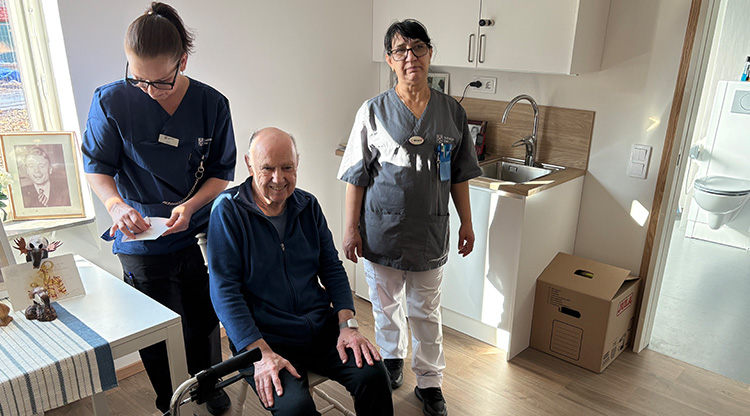 Två personal tillsammans med en brukare i hans lägenhet på ett särskilt boende. Mannen ler och tittar in i kameran. FOTO.