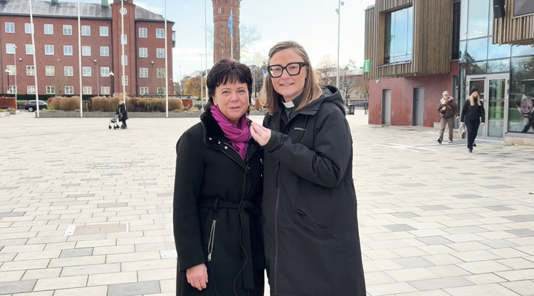 Två kvinnor står på ett torg med en microfon i handen