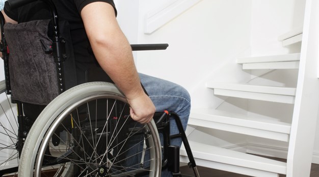 Man i rullstol sitter framför en trappa.