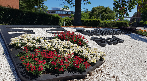 Bilden föreställer en plantering med Trollhättans Stads vapen och namn. I stadsvapnet är det röda och vita blommor.