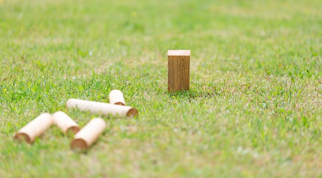 Trämaterial från spelet kubb ligger på en gräsmatta.