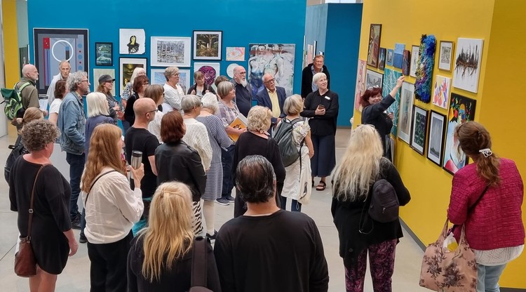 Människor samlade runt olika konstverk i en konsthall.