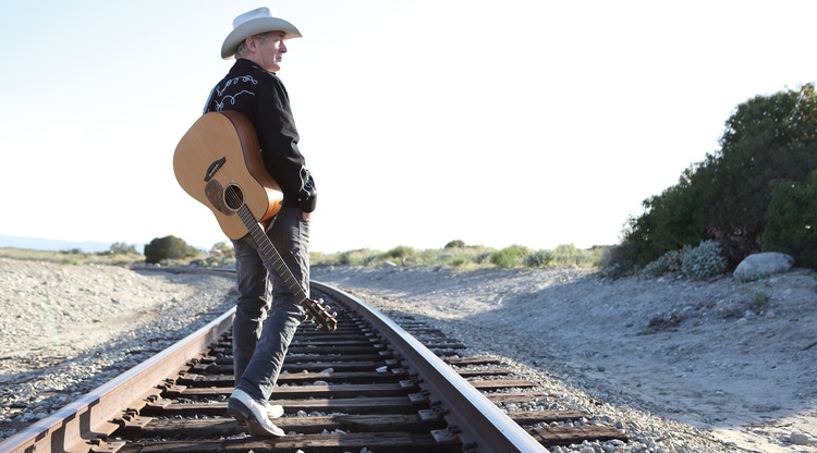 Artisten Doug Seegers promenerar på järnvägsräls med en gitarr.
