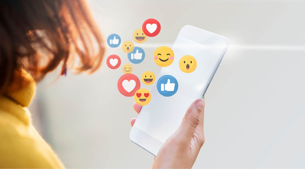 Hand som håller i mobiltelefon där olika emojis poppar ut.