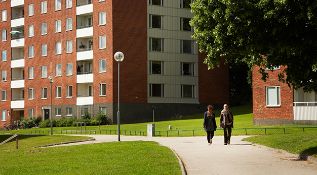 Två personer promenerar utanför ett bostadsområde med lägenheter i flera höghus.