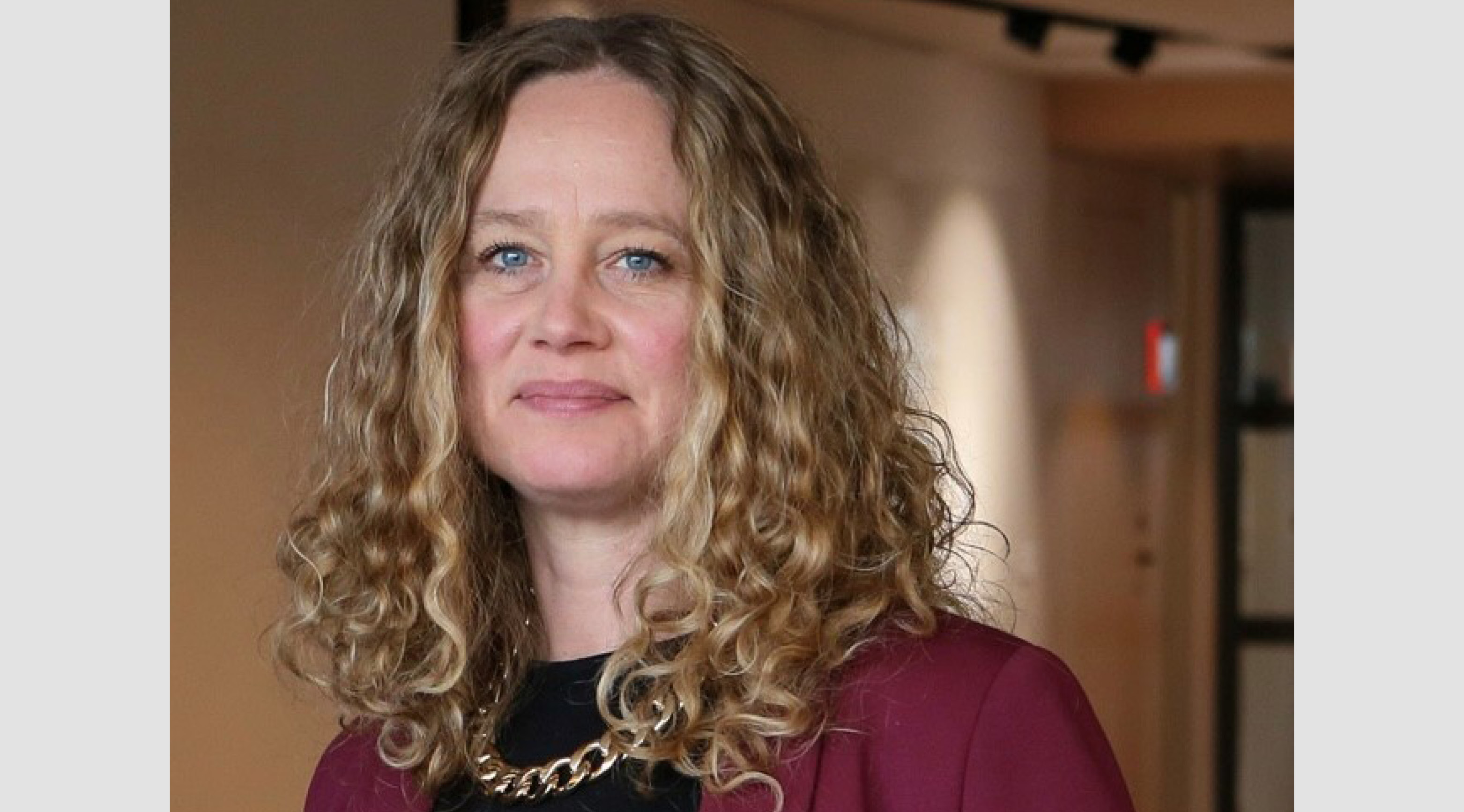 Porträttbild på Elin Johansson. Kvinna med lockigt hår och vinröd tröja. 