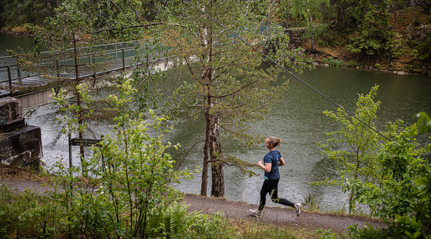 Bilden föreställer en kvinna som springer vid älven. Bilden är tagen i fågelperspektiv så man ser kvinnan uppifrån. Omgivningen är full av grönska, det syns att de precis regnat. Trädens gröna blad riktigt lyser. 