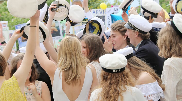 Ungdomar som festar med studentkläder och mössor på sig