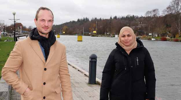 Två personer står utomhus med jackor på en brygga vid kanalen.