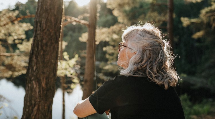 Kvinna blickar ut över sjö och skog samtidigt som solen lyser.