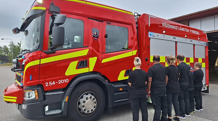 En rad med människor står med ryggen mot kameran framför en brandbil