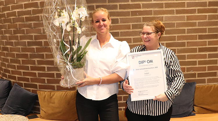 Två tjejer framför en teglevägg håller blomma och diplom.