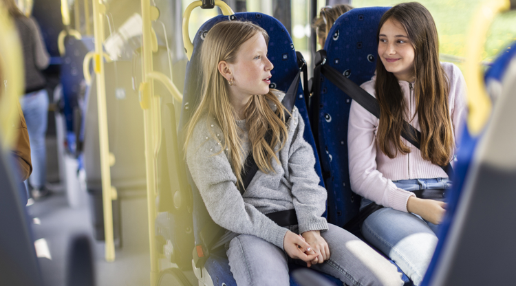 två unga tjejer sitter på en buss, skrattar. 