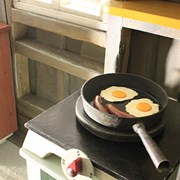 Bilden är en närbild på en spis i en lekstuga. På spisen står en stekpanna med två ägg och två korvar. 