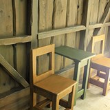 Bilden föreställer två stolar i trä och ett litet grön bord som står mot en vägg. 