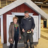 Bilden föreställer kommunalråd Monica Hansson och snickaren Frank Zandhoff utanför en lekstuga som ska placeras på lekplatsen. Frank håller i en stekpanna som ska placeras på stugans spis. 