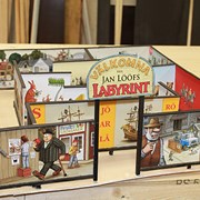 Fotografiet är ett foto på en skiss i miniatyrformat. Skissen föreställer den labyrint som ska byggas till Skrotnisses lekplats i miniatyrformat. Labyrinten är prydd med bilder från Jan Lööfs böcker. 