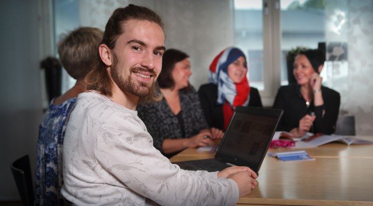 Man med dator och flera människor i bakgrunden