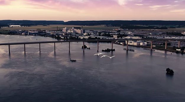 Bilden föreställer Stallbacka området och stallbacka bron. Mitt i bild syns två vita måsar som flyger mot området. Himlen är rosa och lila.