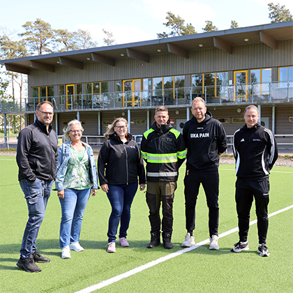 En grupp m&auml;nniskor st&aring;r p&aring; en konstgr&auml;splan.