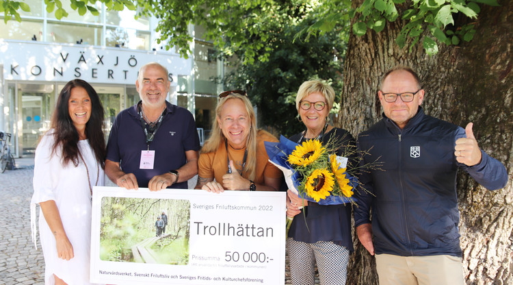 Personer står utomhus med stor check och blommor