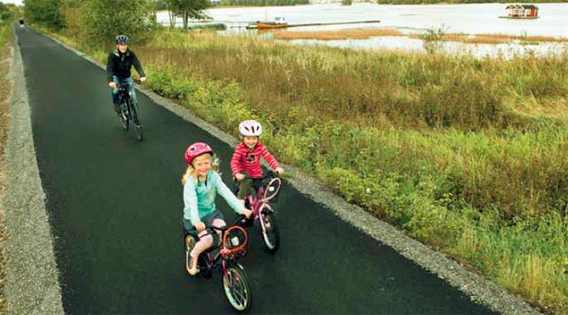 På cykelvägen till Överby cyklar två flickor och en förälder. Alla tre bär cykelhjälm.