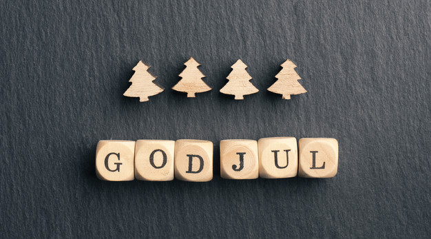 Tärningar med texten God Jul samt 4 trädgranar mot en grå bakgrund