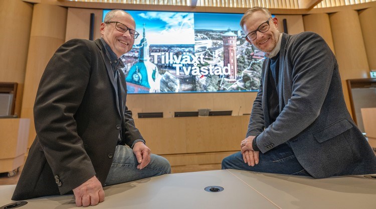 porträtt, två män sitter på ett bord, tittar in i kameran och ler. 