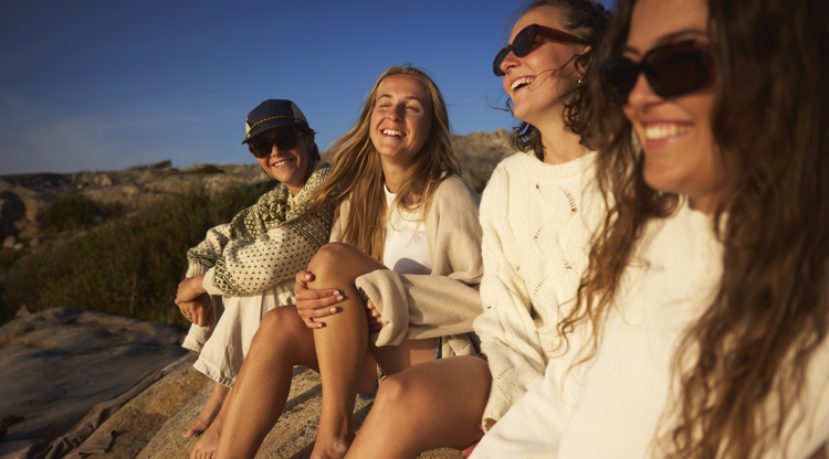 ungdomar sitter på en klippa och skrattar, solnedgång och hav. 