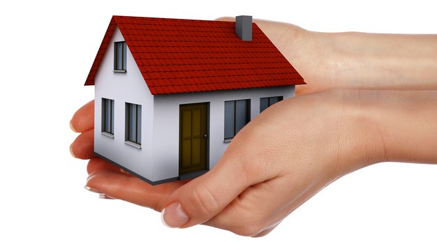 fotografiet är en grafisk bild över två händer som håller i ett litet hus med rött tak. 