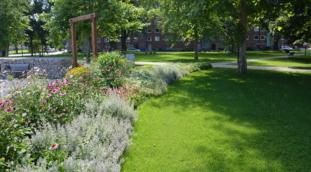 Fotografiet är ett foto över en park. I bildens vänstra hörn löper en stor rabatt med flera olika former av blommor och buskar i alla möjliga olika färger. Denna rabatt löper från fotots vänstra hörn till mitt i bild. Till höger i bild är det en gräsmatta. I bakgrunden syns grusgångar och flera stora gräsytor. 