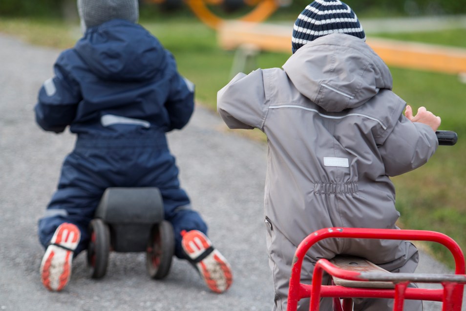 Foto av två små barn i overaller som cyklar bort från kameran.